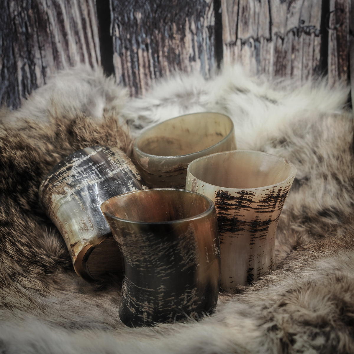 Set om fyra handsnidade whiskyglas av horn med naturlig yta, olika hornfärger, på träbasar, presenterade tillsammans