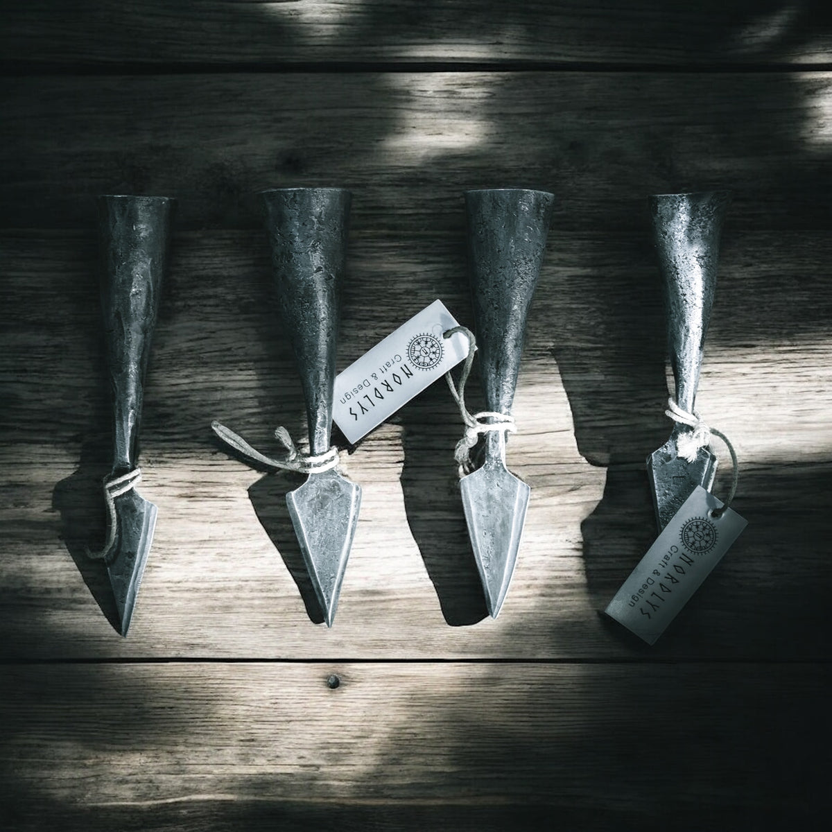 Fyra identiska smiderade järnspjuthållare uppsatta i rad på trä, alla med märk, visande sätet innehållet