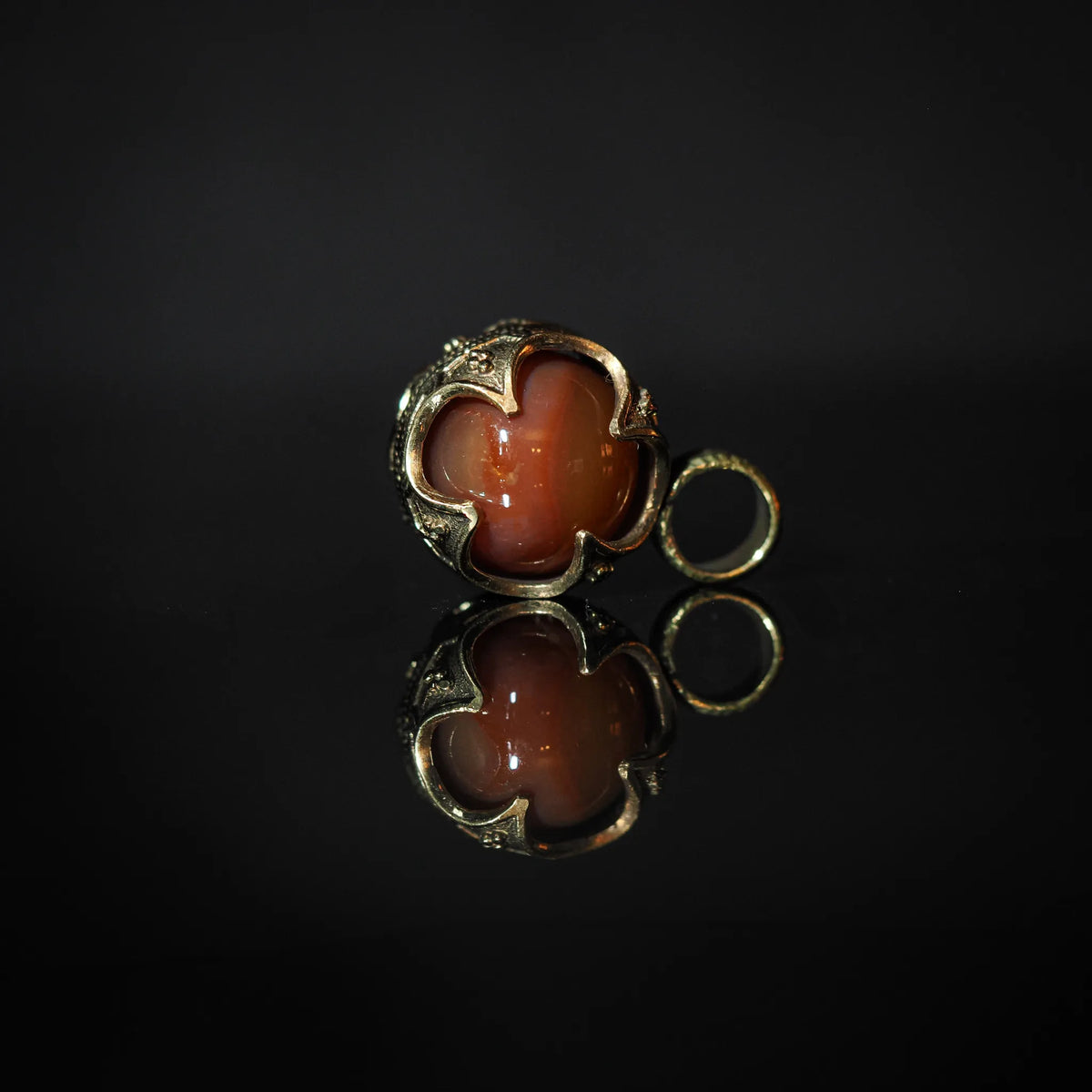 Två rödbruna agathangar med ornerad silverpläterad metall i vikingastil. Symmetriska halvmåneformade kapor med glansiga stenor och små lösa ringar bredvid.
