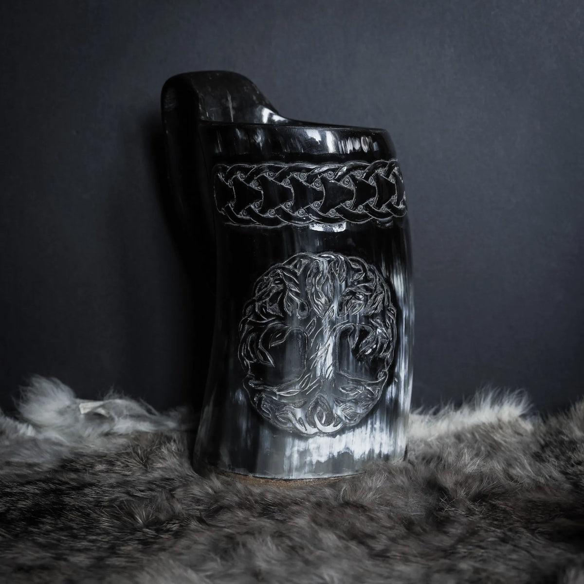 Handsnidad hornmugg med Livets träd i centrum och vikingaknut-band. Svart polerad horn med djupa huggningar. Keltisk flätmönster överst på muggen. Kraftig båge-formad handtag.