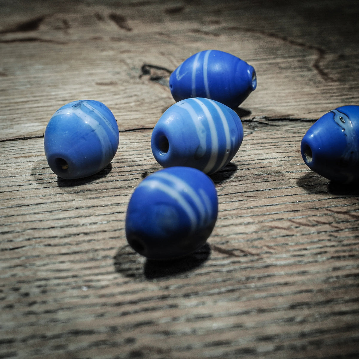 Blue elongated glass bead with white stripes. Uppsala