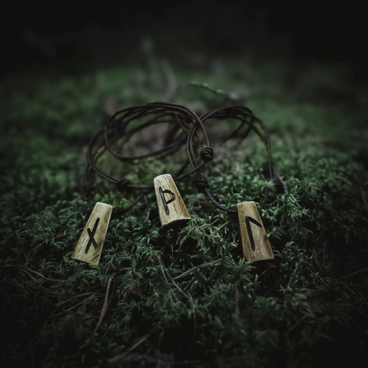 Handgjord runhalsmycke med tre rektangulära benmycken snidade med nordiska runor. Svart läderrem. Fotograferat på naturlig mossbakgrund. Traditionellt vikingainspirerat smycke för män och kvinnor.