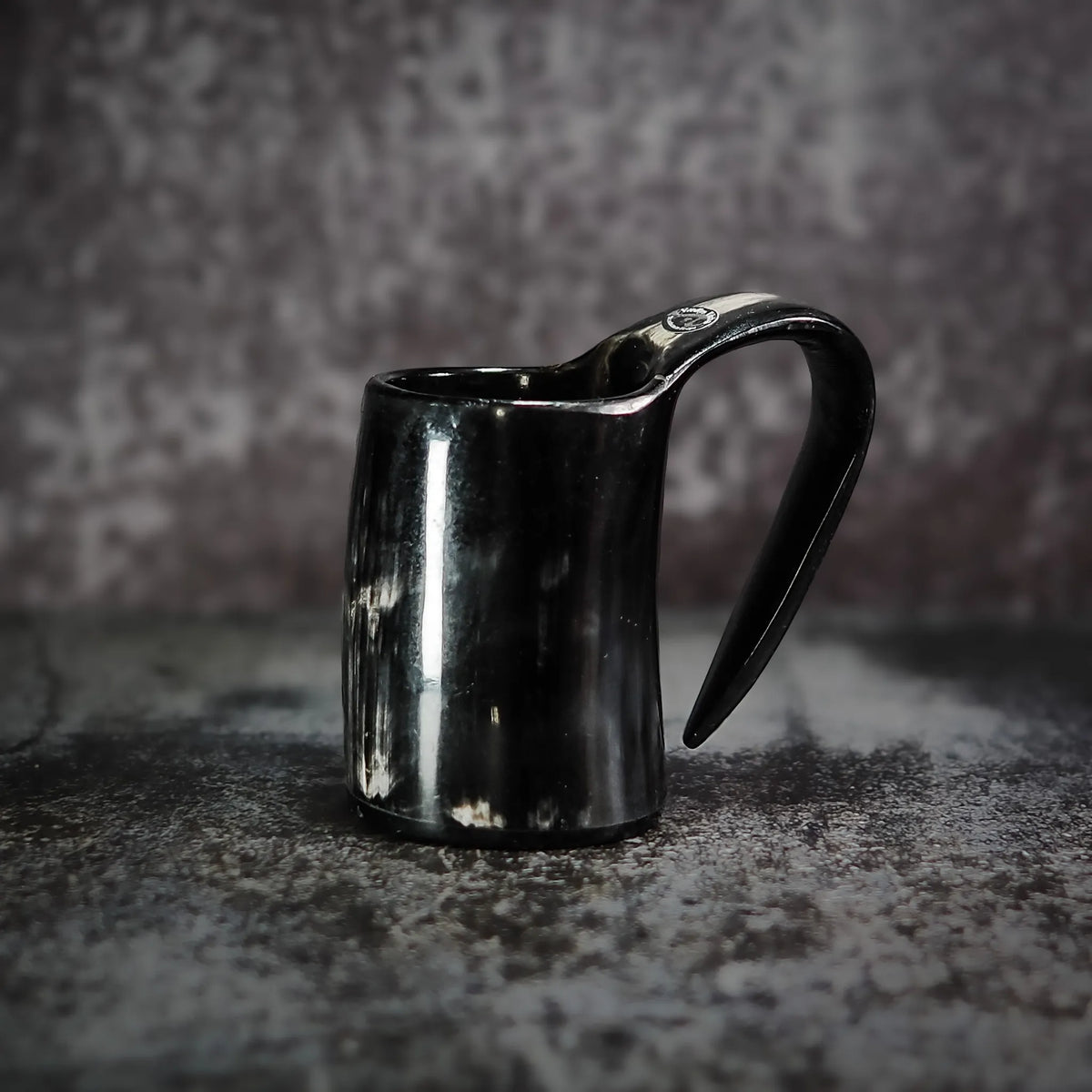 En handgjord espresso- och glöggmugg i horn med naturlig textur och polerad svart yta, fotograferad på grå betong.