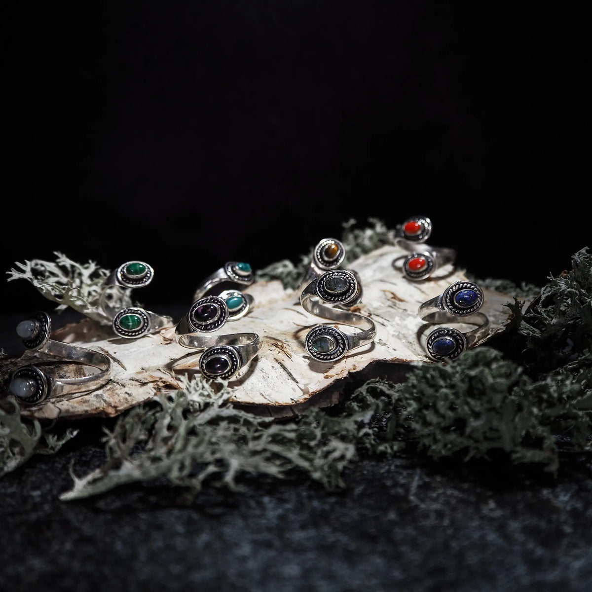 Flera justerbara spiralringar med labradorit halvädedelstenar som glimmrar i norrskenets färger på väder drivved och lav.