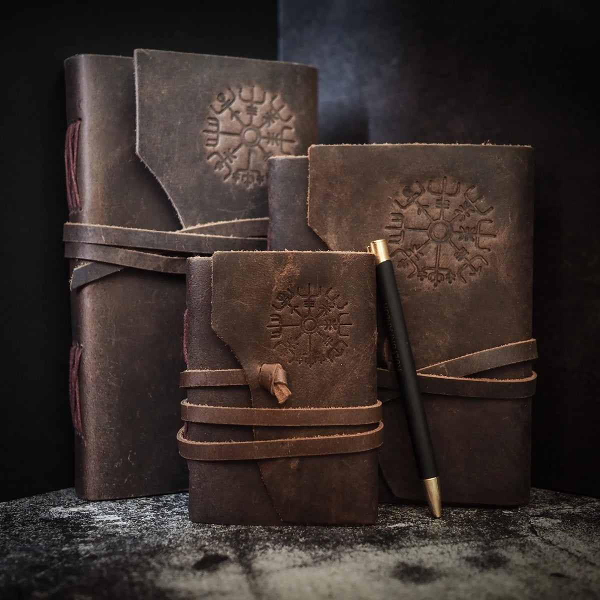 Three leather notebooks in varying sizes with embossed Vegvisir Norse compass symbols, dark brown leather with tie straps