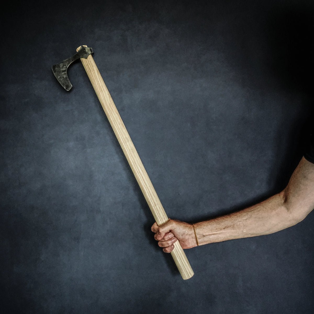 Bearded axe for blunt-weapon fighting – the axe raised in hand, profile against a dark background