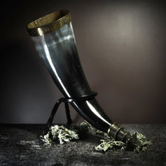 Polerat bärskärhornkärl med naturhorn, mässingskant och svart metallställ med tre ben, visar Viking-inspiration