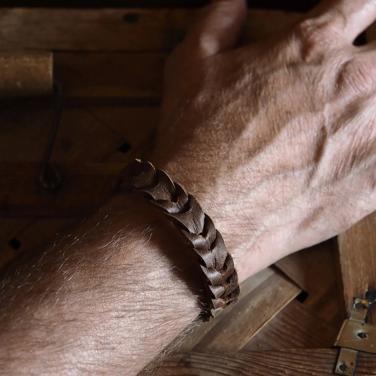 Närbild av ett mörkbrunt flätat läderarmband på en mans handled, med synlig spiralmönstrad vävdesign och naturlig läderpatina