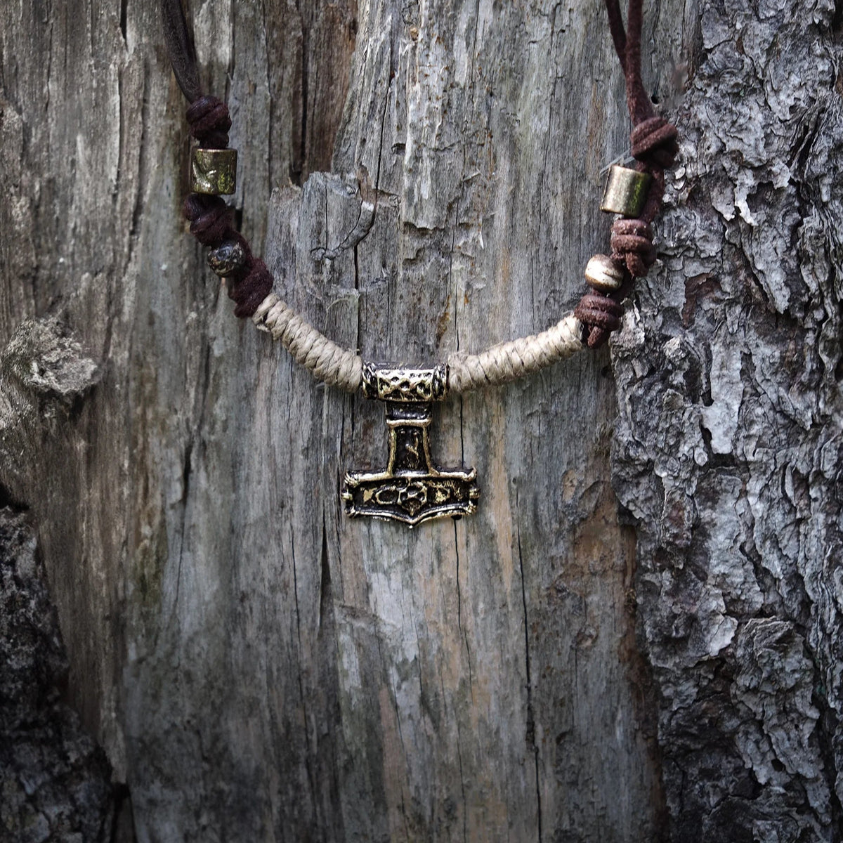 Mjölner-halsband i brons fotograferat utomhus mot grön bokeh-bakgrund. Bronshammare med detaljer synligt på läderband.