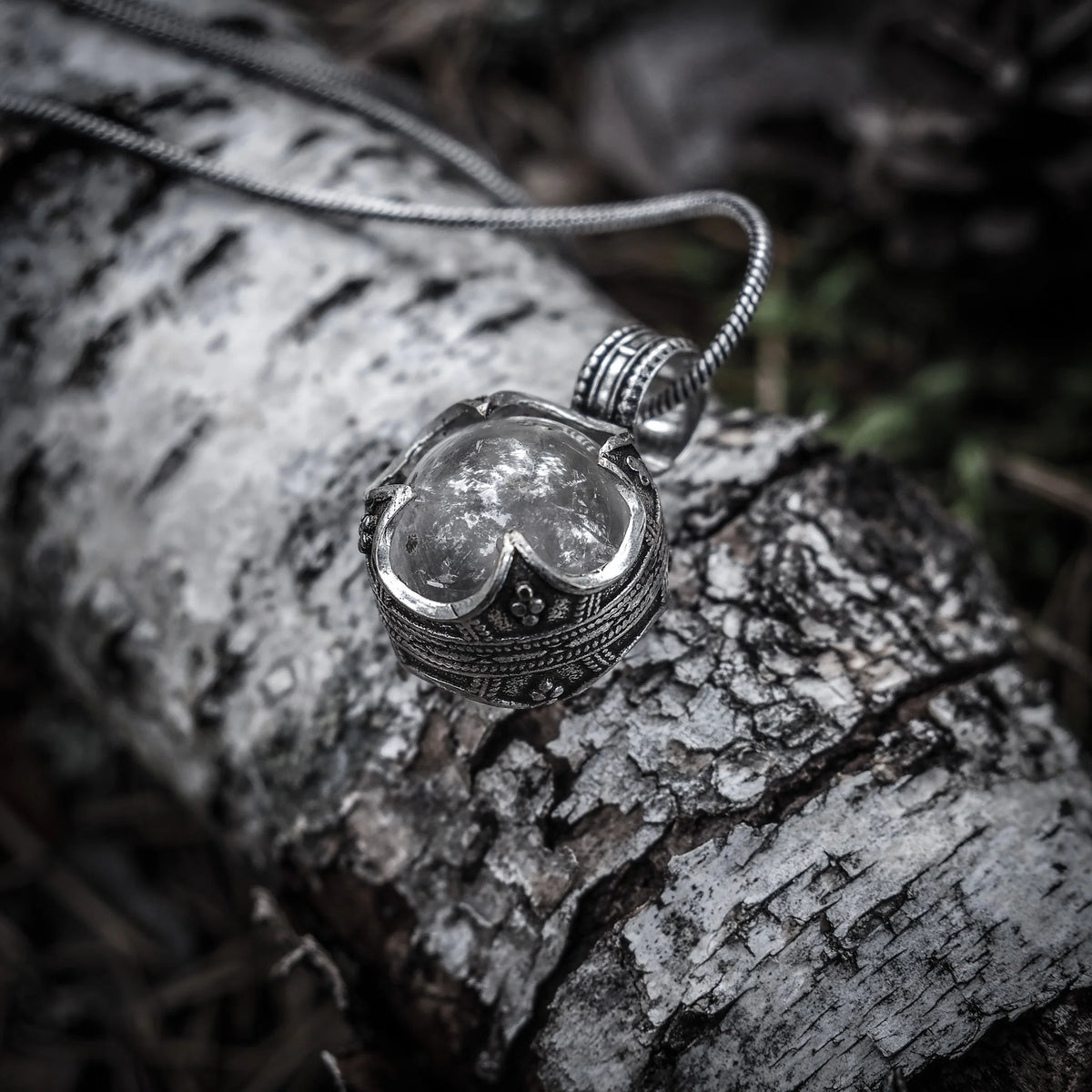 Gotlandshänge med bergkristall i silverglans på silver kedja, fotograferad mot naturlig skogsmiljö med mossa täckt ved
