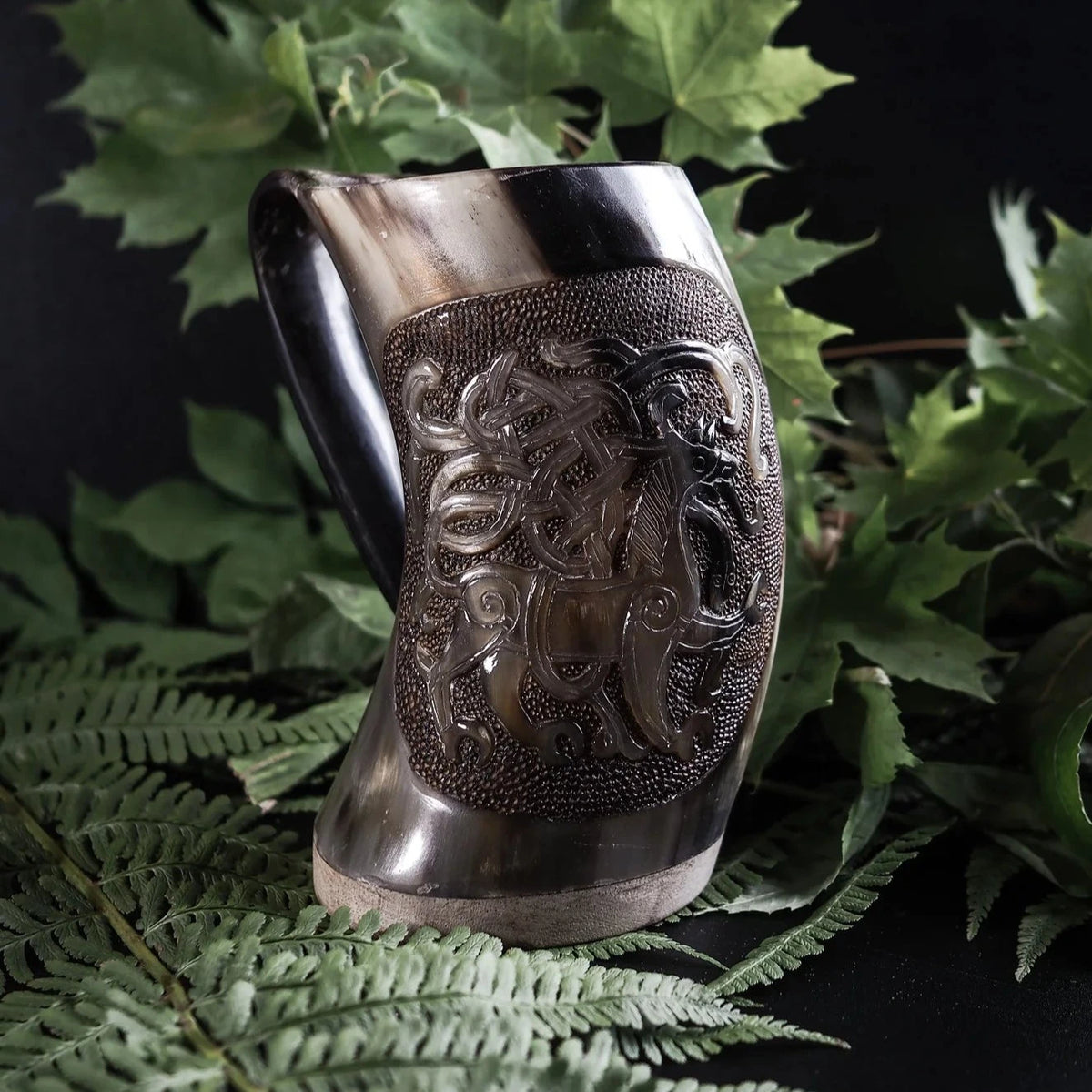 Hornmugg med Mammen varg-motiv i ljus variant. Mässingsinsats visar intrikat invävd vargteckning med karakteristisk Mammen djurstil. Prickad textur omger huvudgestalten. Naturligt horn med fin kornstruktur.