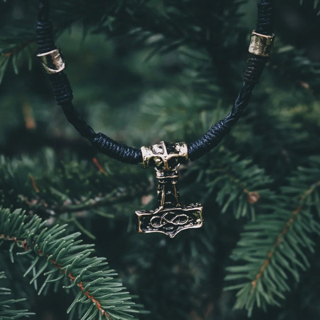 Torshammare Öde-halsband med grovt flätad lädersnöre och Mjölnir-anhängare mot naturlig grön bakgrund, handgjord