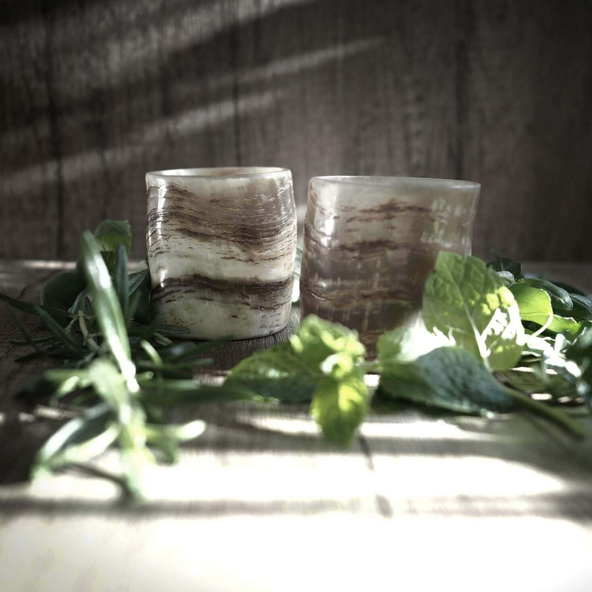 Närbild på två whiskyglas av horn med naturlig yta, ljus hornfärg med naturlig struktur, på träbasar