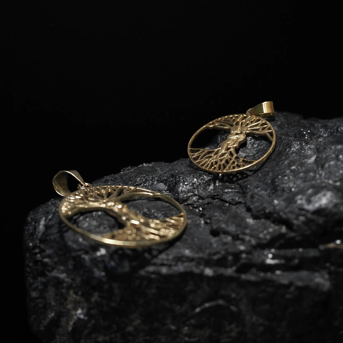 Stor träd-amulett i mässing/guld fotograferad på mörkgrå sten, visar Yggdrasil med synliga grenar och rötter.