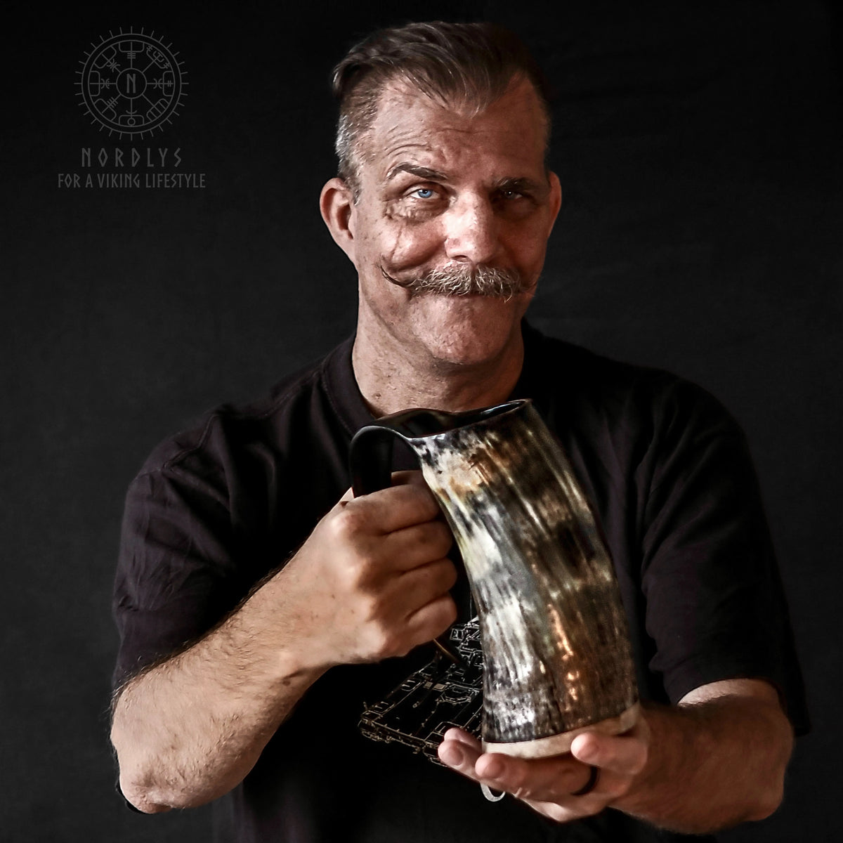 Skäggig man med mustasch håller stor Tor-mugg (700-900ml). Bär svart t-shirt med Nordlys-logga. Mottlad hornfärg synlig.