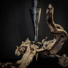 Smiderad järnspjuthållare bland torkade växter och trä, visar metallarbetets textur och spetsiga design