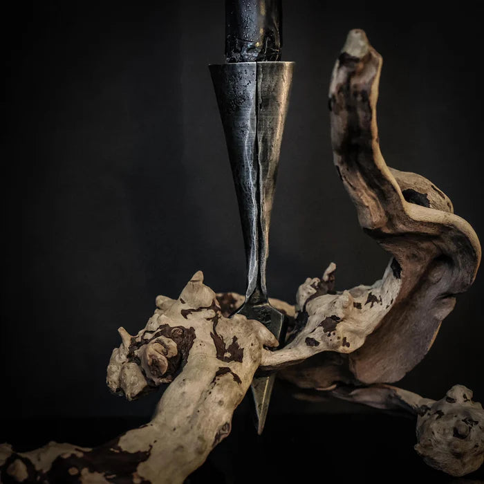 Smiderad järnspjuthållare bland torkade växter och trä, visar metallarbetets textur och spetsiga design