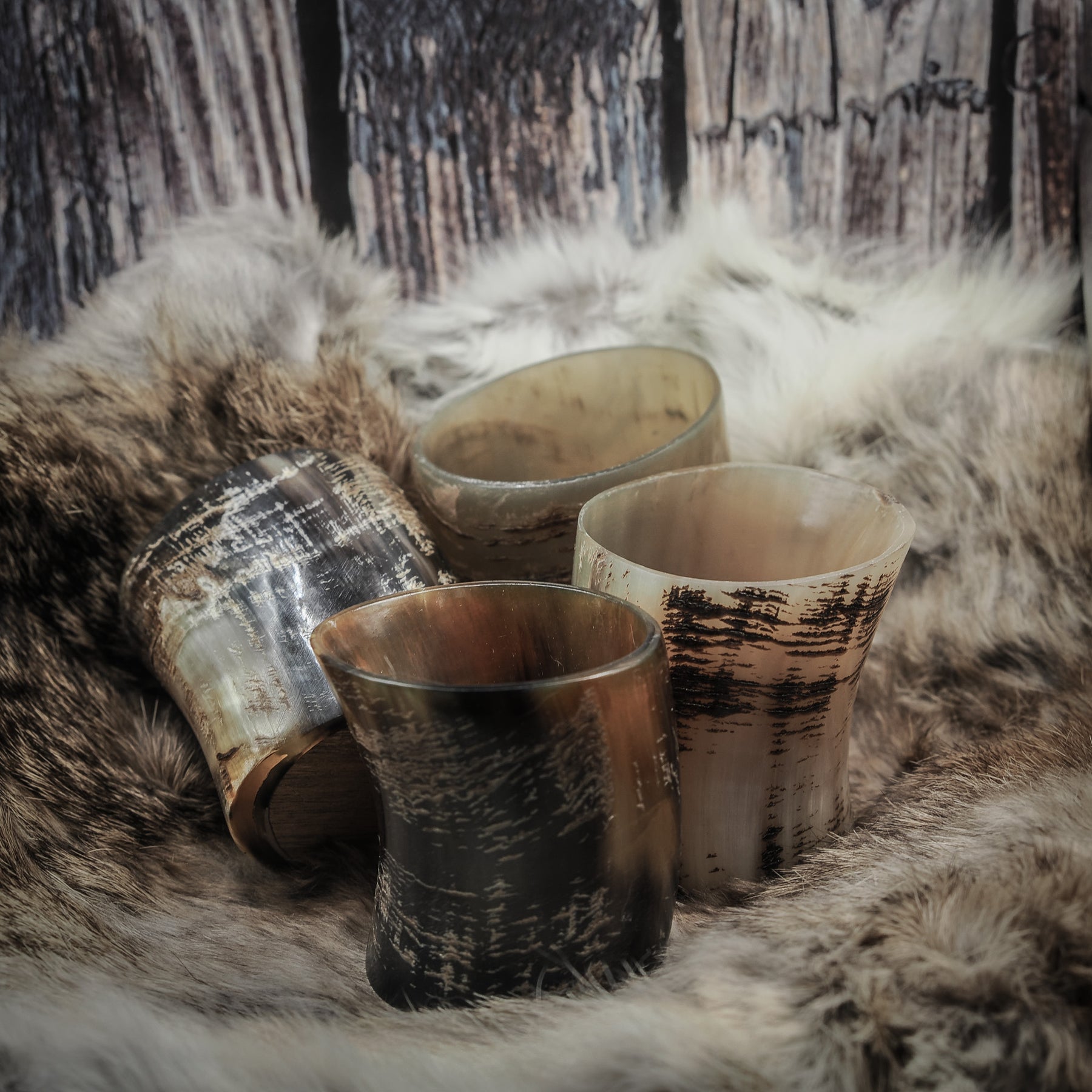 Set om fyra handsnidade whiskyglas av horn med naturlig yta, olika hornfärger, på träbasar, presenterade tillsammans