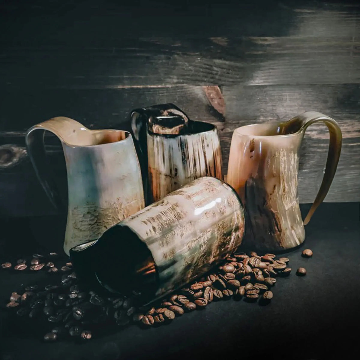 Fyra ljusa hornkaffemuggar med mässingshandtag på mörkt trä.