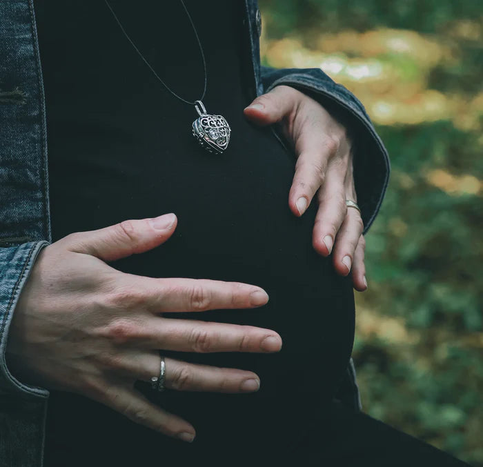 En silverfärgad änglaklocka (änglaklocka) med ornerad design hållen mot mörka kläder, visar smyckets storlek och detaljer.