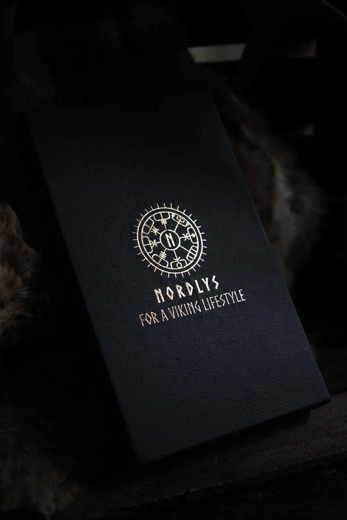 Presentaskdetaljfoto med präglad vikingrune och Nordlys varumärkestext 'FOR A VIKING LIFESTYLE' på svart matt material