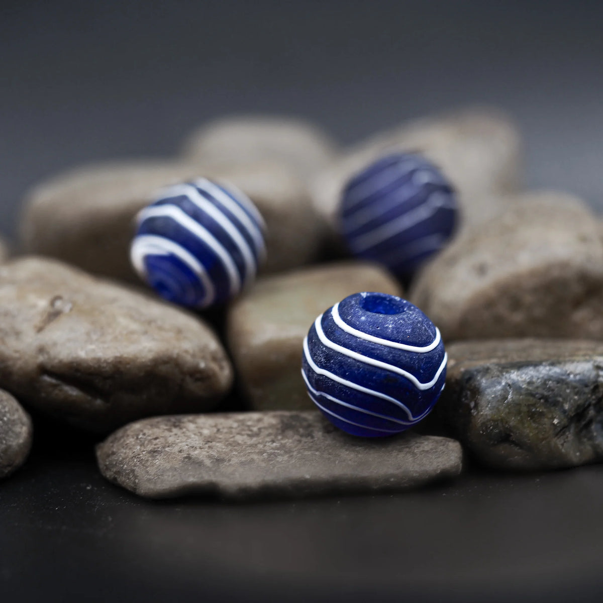 Frostad blå glaspärla med vit dekoration fotograferad på natursten visar matt finish och stripedesign