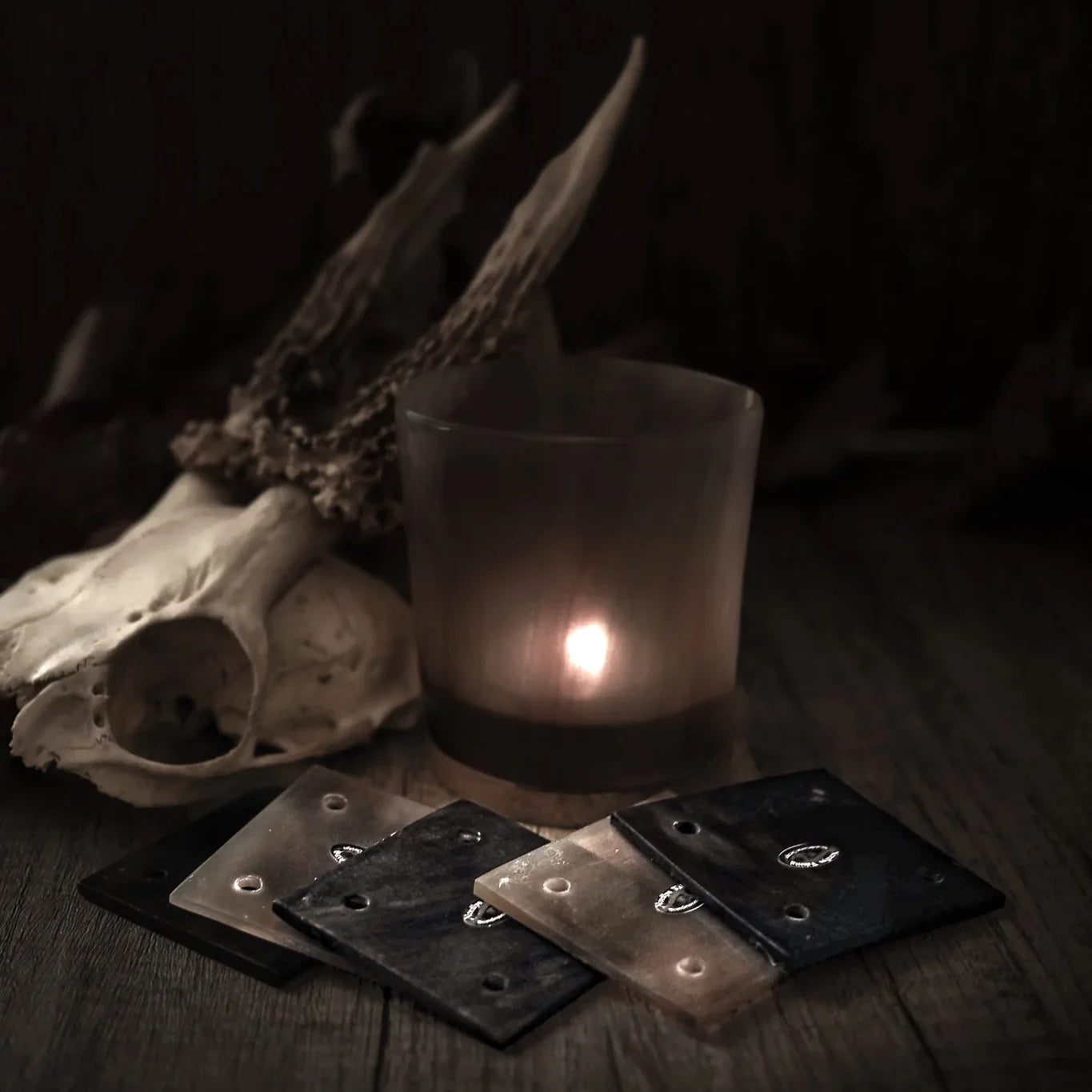 Tre hornbrickor för brickväv uppställda på mörk yta med djurkranium i bakgrunden och brinnande ljus, arrangerad för att visa traditionella vikingweaving-verktyg