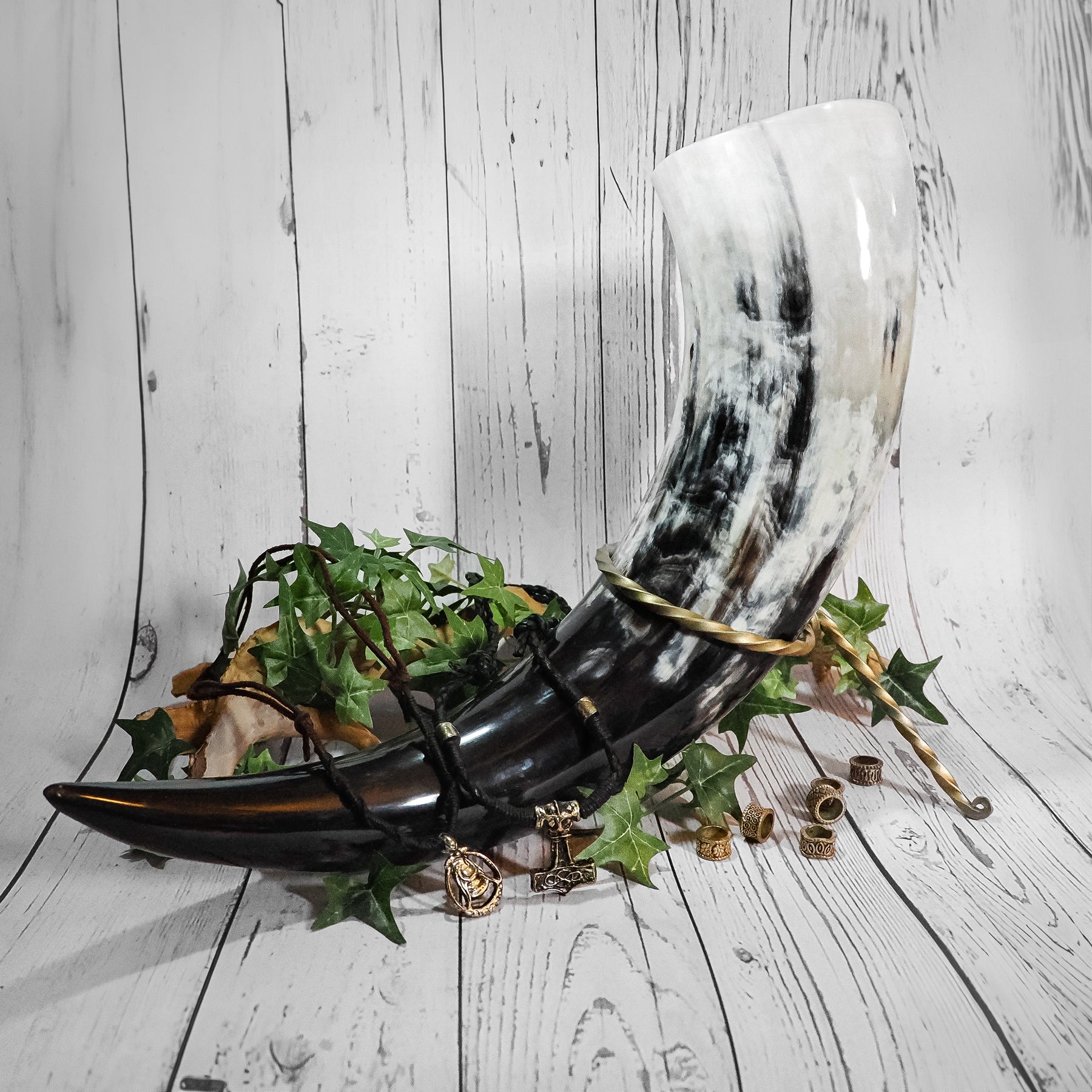 Fullständigt vikingbröllopspaket utlagt på träyta - dryckeshorn, hornhållare, lädersmycken med vikinganhängar, hårperler och växtdekoration