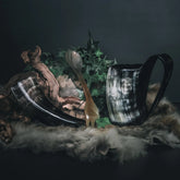 Camping-kit med två hornmugg och träkål, dekorerad med växter och moss på mörkgrön bakgrund