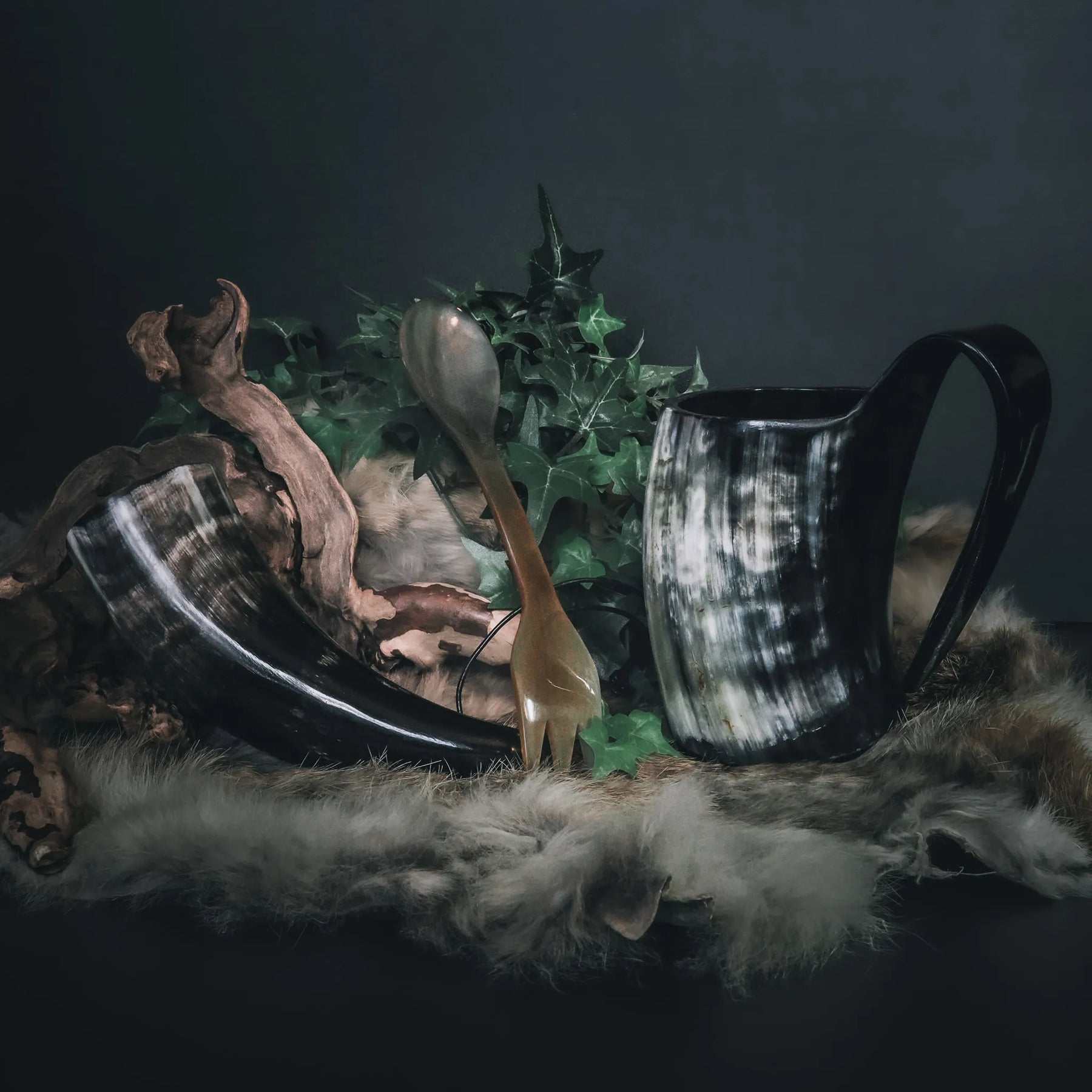 Camping-kit med två hornmugg och träkål, dekorerad med växter och moss på mörkgrön bakgrund