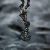 Halsband Enride - Torshammaren från Mickels med antikt mynt, upphängt i mörk läderband. Fotografi mot stormig oceanvågbakgrund som inspirerar vikingatmosfär.