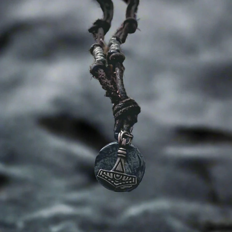 Halsband Enride - Torshammaren från Mickels med antikt mynt, upphängt i mörk läderband. Fotografi mot stormig oceanvågbakgrund som inspirerar vikingatmosfär.