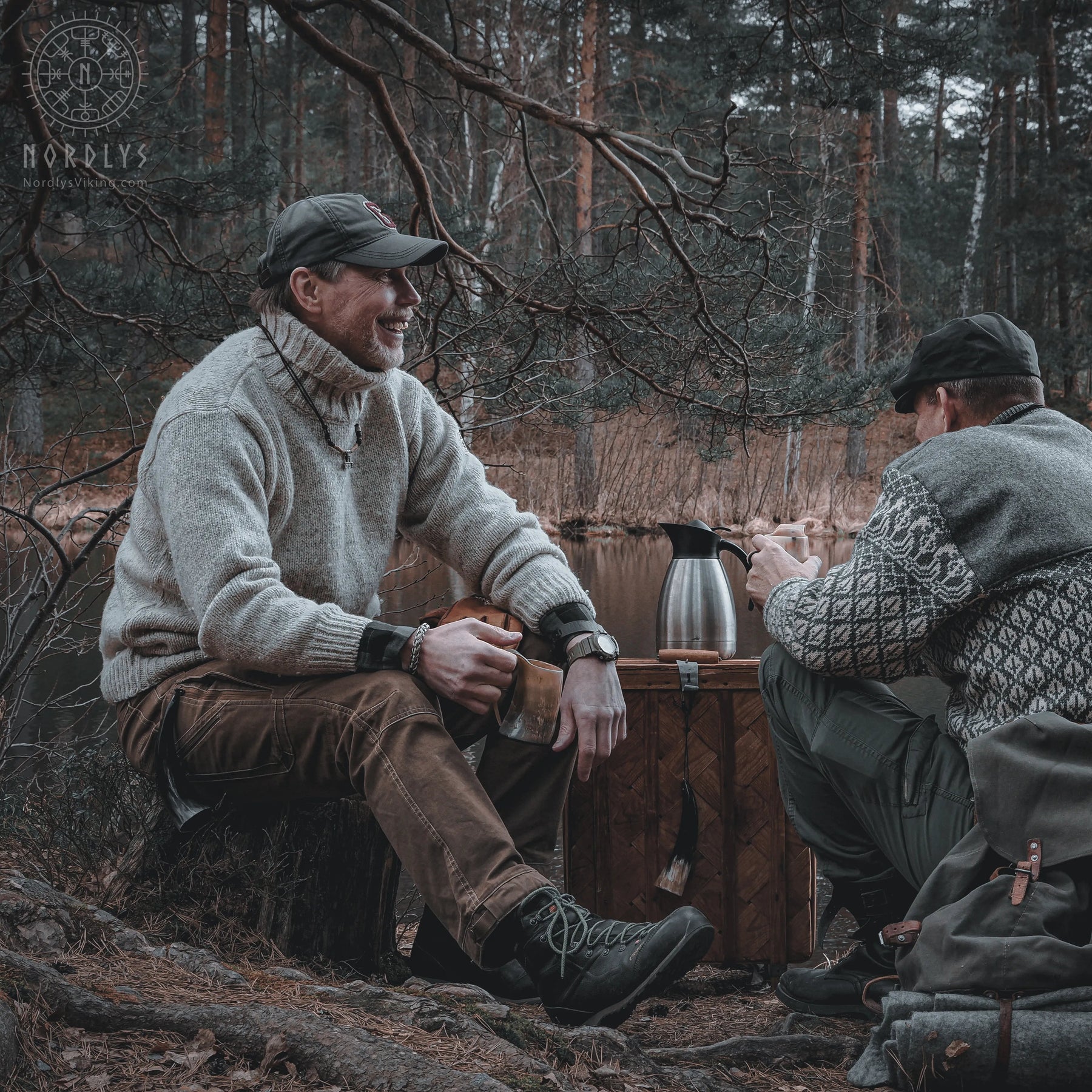 Två män i skogsmiljö, en med grå tröja håller polerad hornmugg, Nordlys logotyp synlig, höst/vinterscen