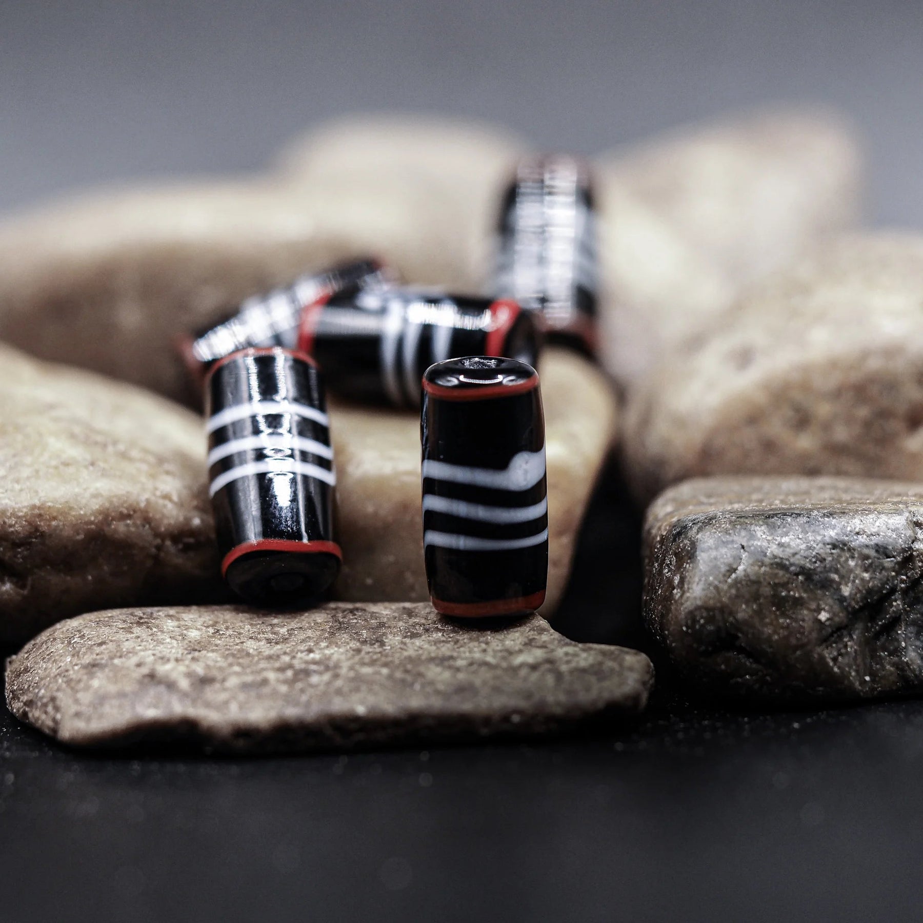 Svart glaspärla med grå och röd dekor - cylindrisk form från Ribe, Danmark. Vikingatida handelspärla med geometriska ränder.
