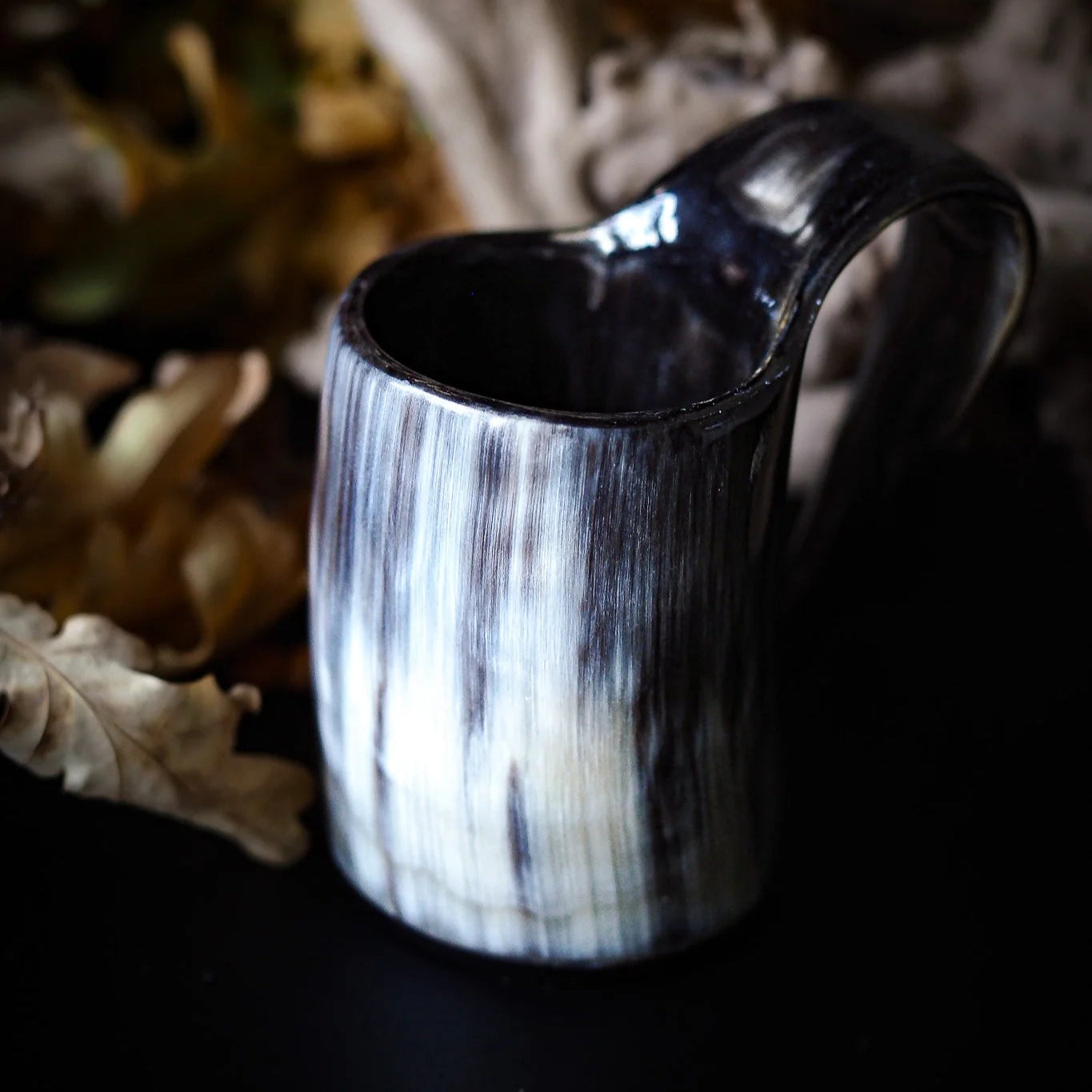 En ljus hornad mugg med naturliga kornmönster och böjd handtag, placerad framför en suddig bakgrund med dekoration