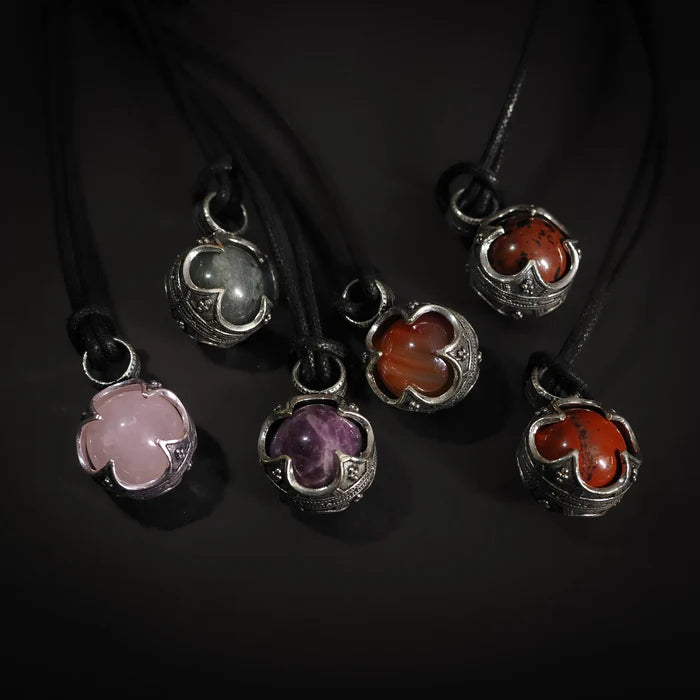 Sex silverpläterade Gotlandskula-hängen med halvädla stenar i olika färger hängande på svart lädersnöre mot mörk bakgrund