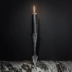 Smiderad järnspjuthållare för ljus med tänd ljusslåga, placerad vertikalt på trä mot mörk bakgrund