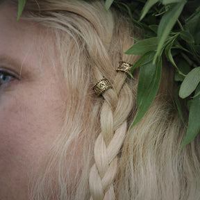 Närbild av två vikingha­rperler med guldiga knotwork-mönster inväva i blont hår