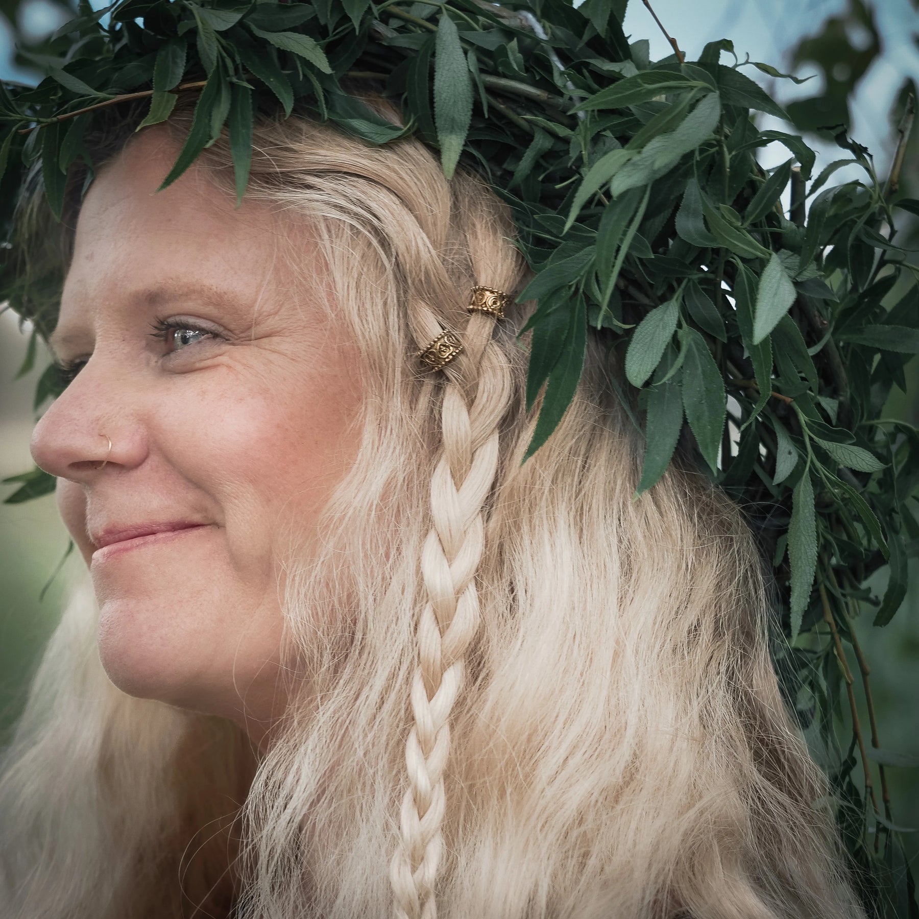 Kvinna med långt blont hår i vikingflätning prydd med guldiga dekorativa hårperler med vikingmönster, sett från sidan