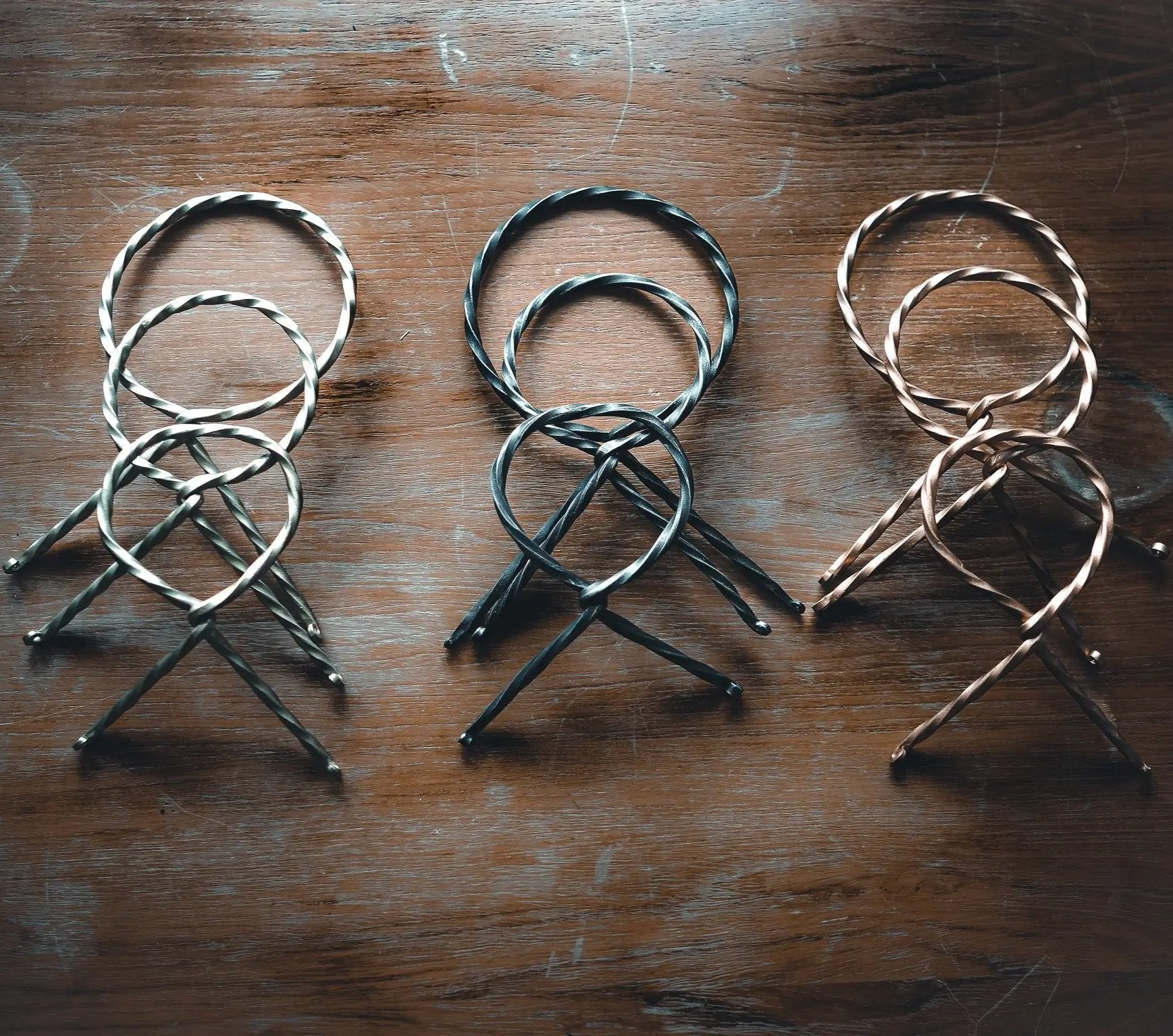 Tre järnsmide-hornstativ i olika färgfinisher visade i rad, alla med samma tredelad design