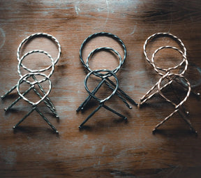 Tre järnsmide-hornstativ i olika färgfinisher visade i rad, alla med samma tredelad design