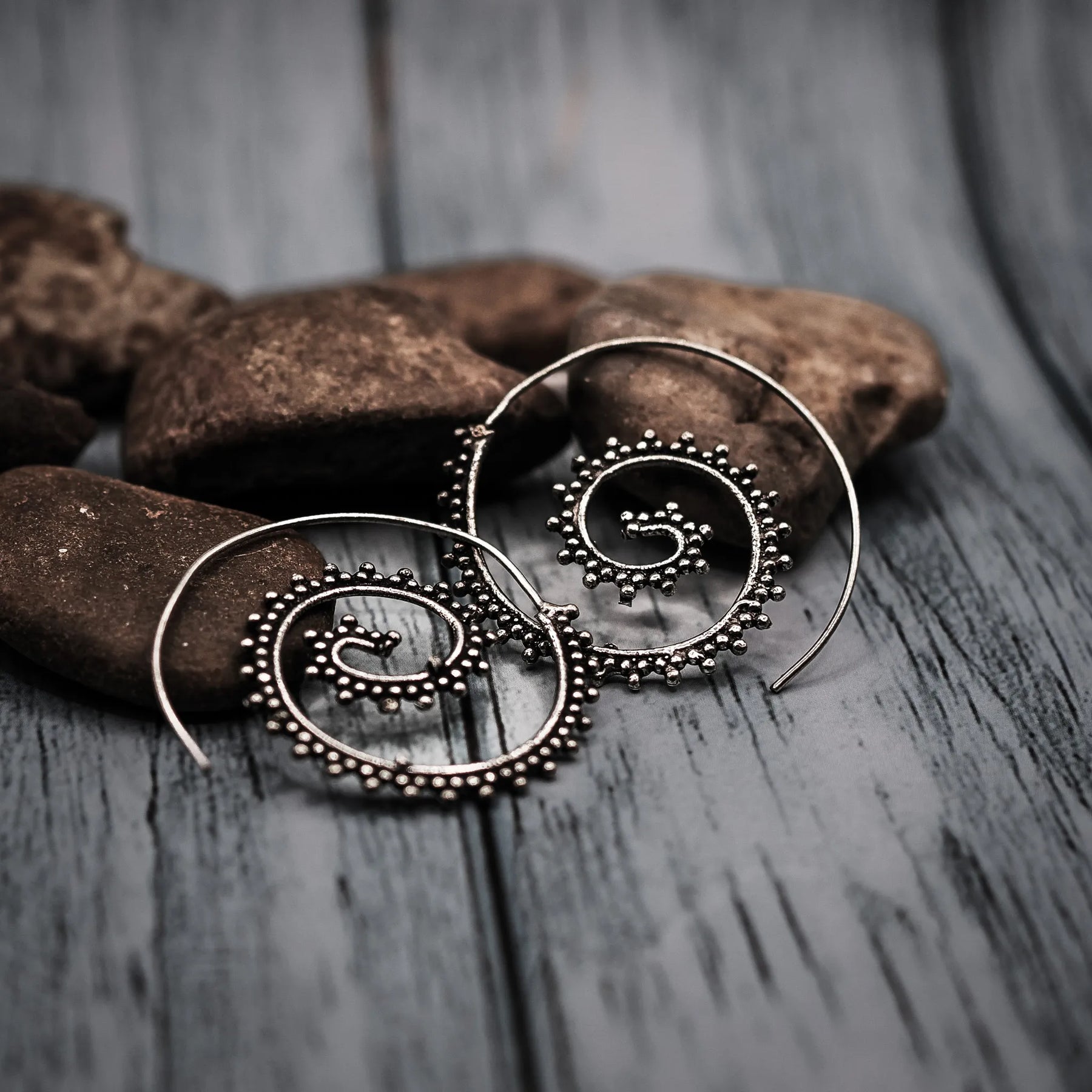 Stora silverörhängen med spiralmönster och dekorativa spiraldroppar på naturlig fiberbakgrund