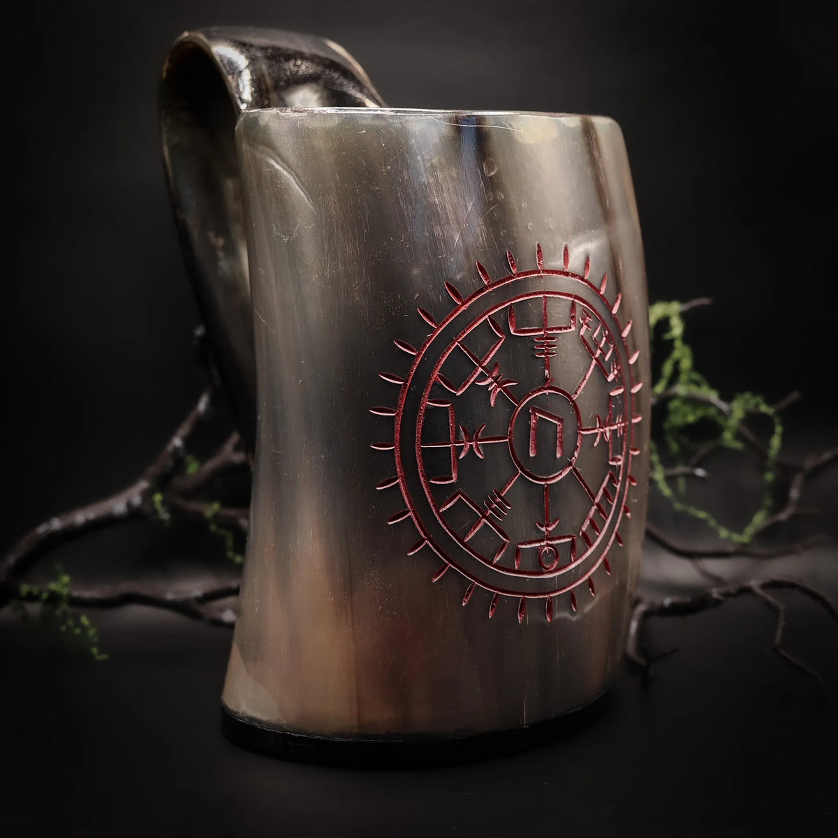 Ölmugg i polerat horn med rödgraverad Vegvisir-kompass, mot mörk bakgrund med kvistar och lav