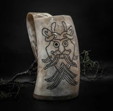 Ljus ölmugg i horn med graverat Odensmask-ansikte i nordisk stil, dekorerad med kvistar och mossa