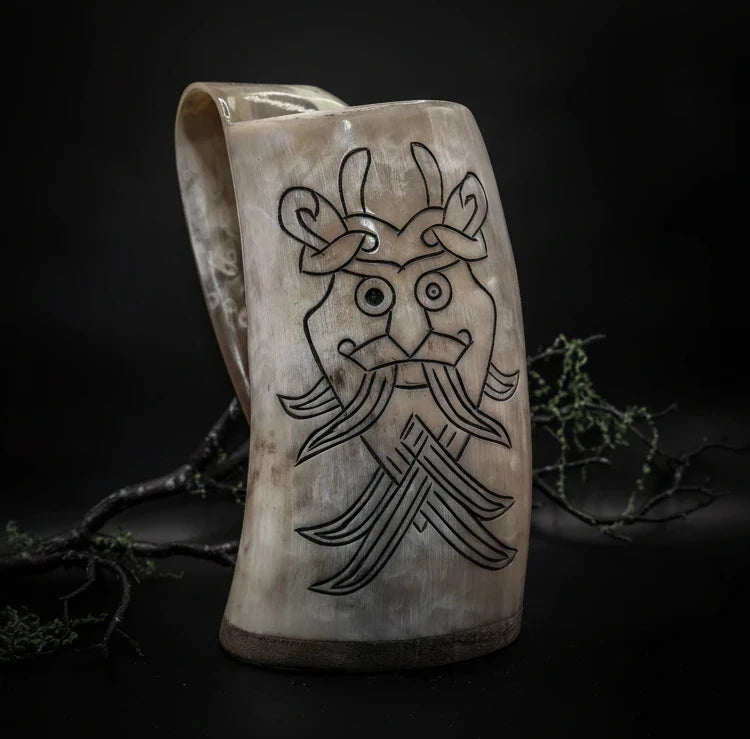 Ljus ölmugg i horn med graverat Odensmask-ansikte i nordisk stil, dekorerad med kvistar och mossa