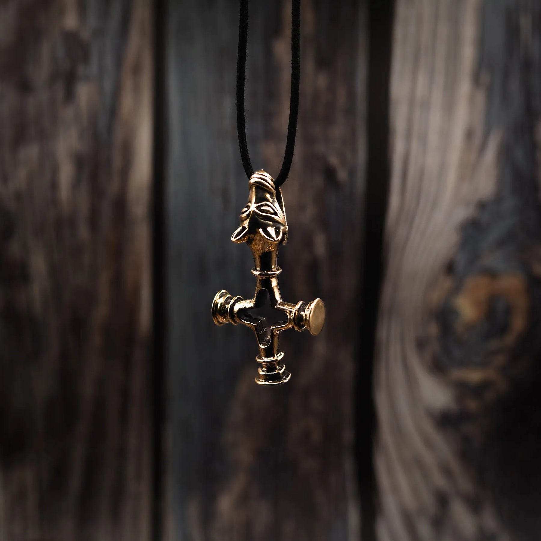 Bronze Vargkors (wolf cross) Viking pendant hanging from black waxed cord against wood background