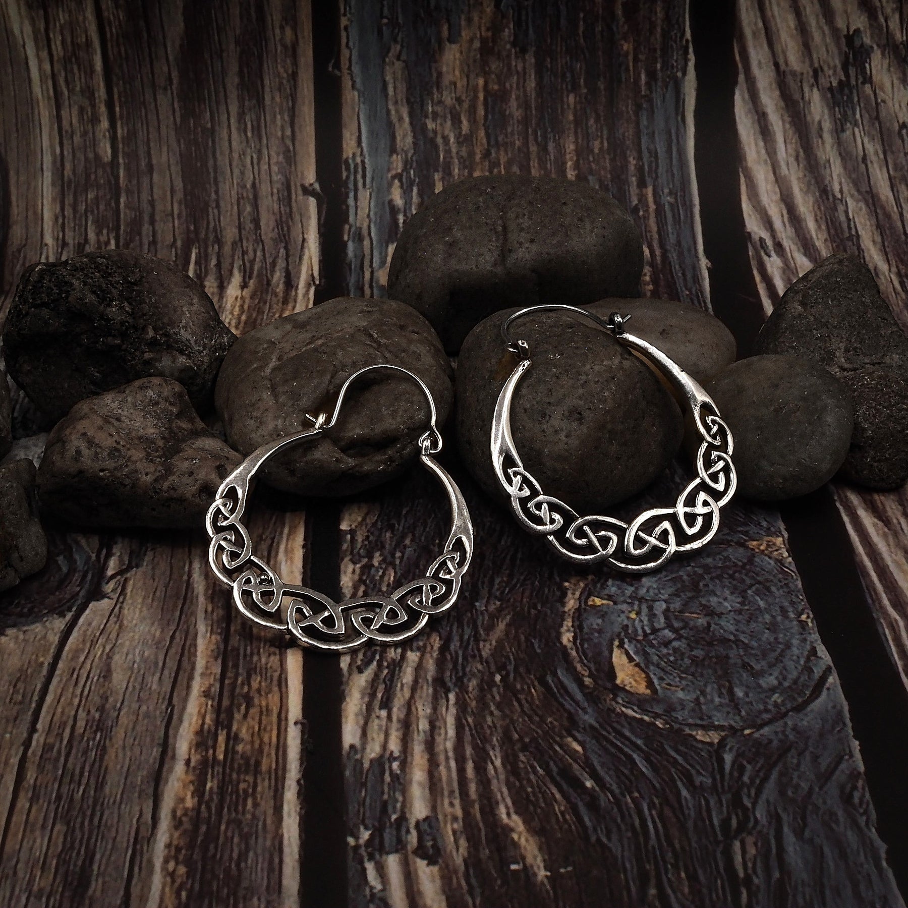 Två keltisk-inspirerade örhängen med flätad knutdesign. Metallarbete visar fina detaljer i det sammanvävda mönstret på trä och stenar.