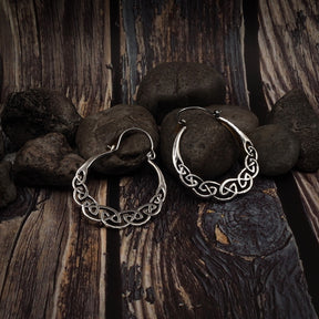 Två keltisk-inspirerade örhängen med flätad knutdesign. Metallarbete visar fina detaljer i det sammanvävda mönstret på trä och stenar.