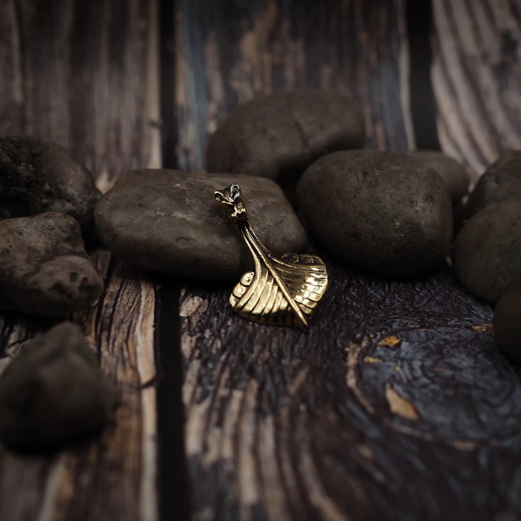 Bronshänge i form av vikingaskepp på träyta. Detaljerad drakehuvud och skeppskrov i metallform med varm glans.