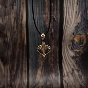 Vikingaskepp-hänge i brons i frontvy mot träbakgrund med runor. Tydlig drakehuvud och skeppskrov i metallguss.